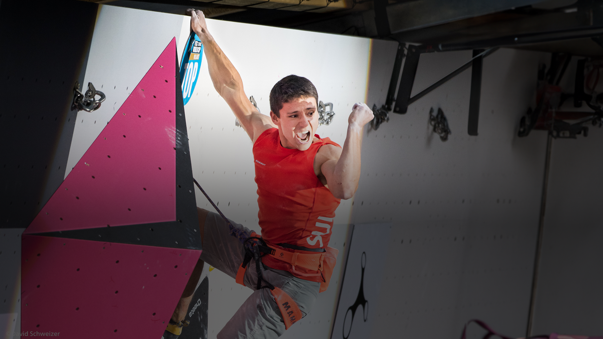 Sascha Lehmann sur le mur d'escalade, affichant une expression triomphante et un geste de victoire